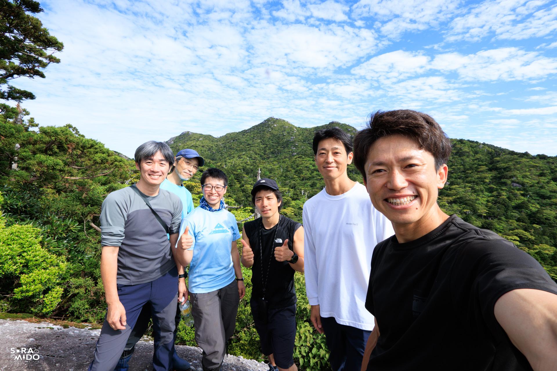屋久島・永田岳へ向かう途中、青空の下で笑顔を見せるガイド仲間6人の集合写真。